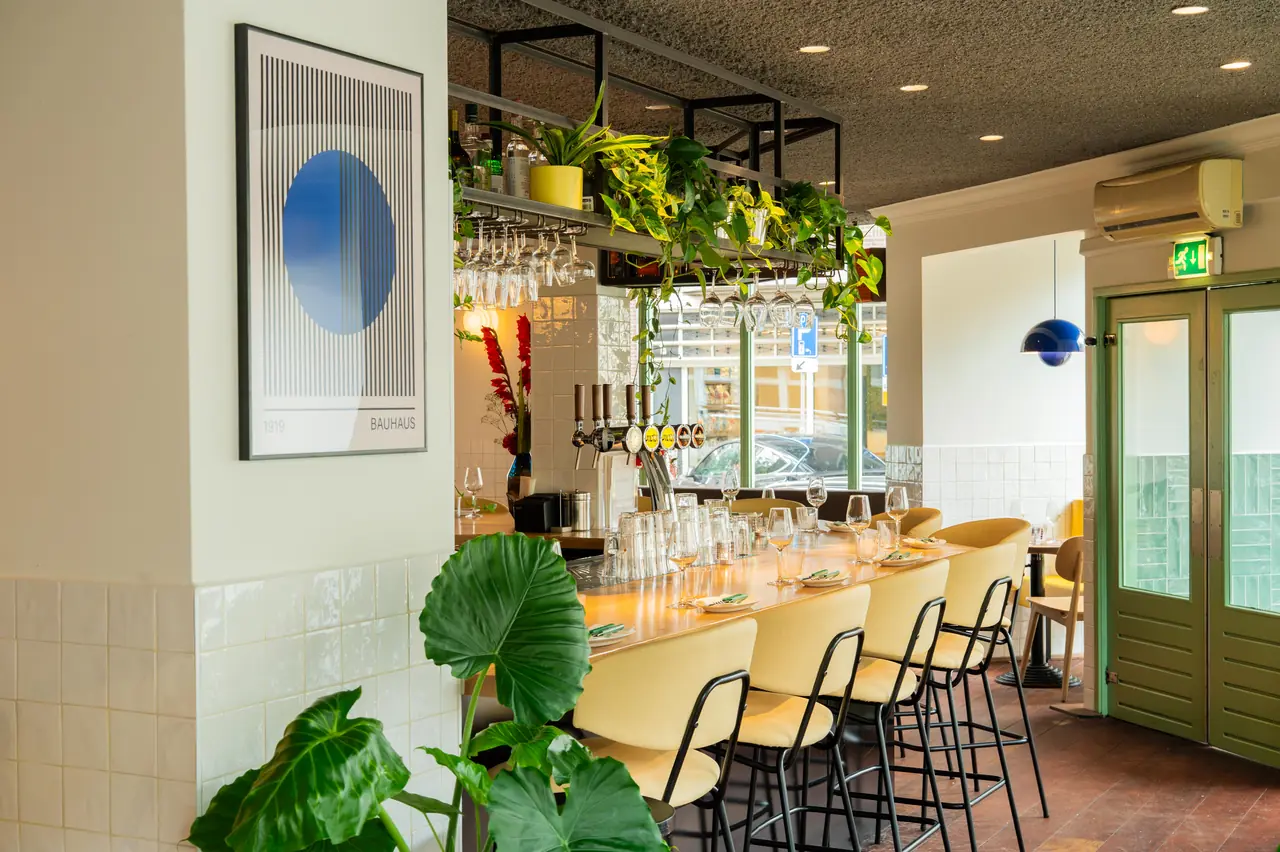 Bar stools along the counter, with plants and a Bauhaus print on the wall